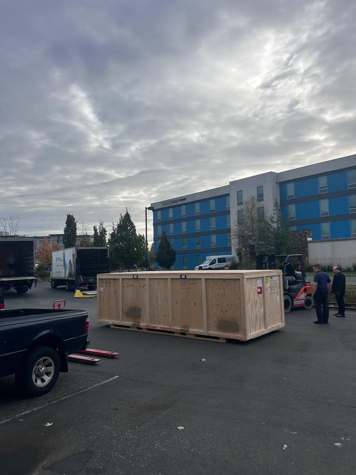 A large wooden shipping crate being unloaded beside a forklift during the printer delivery